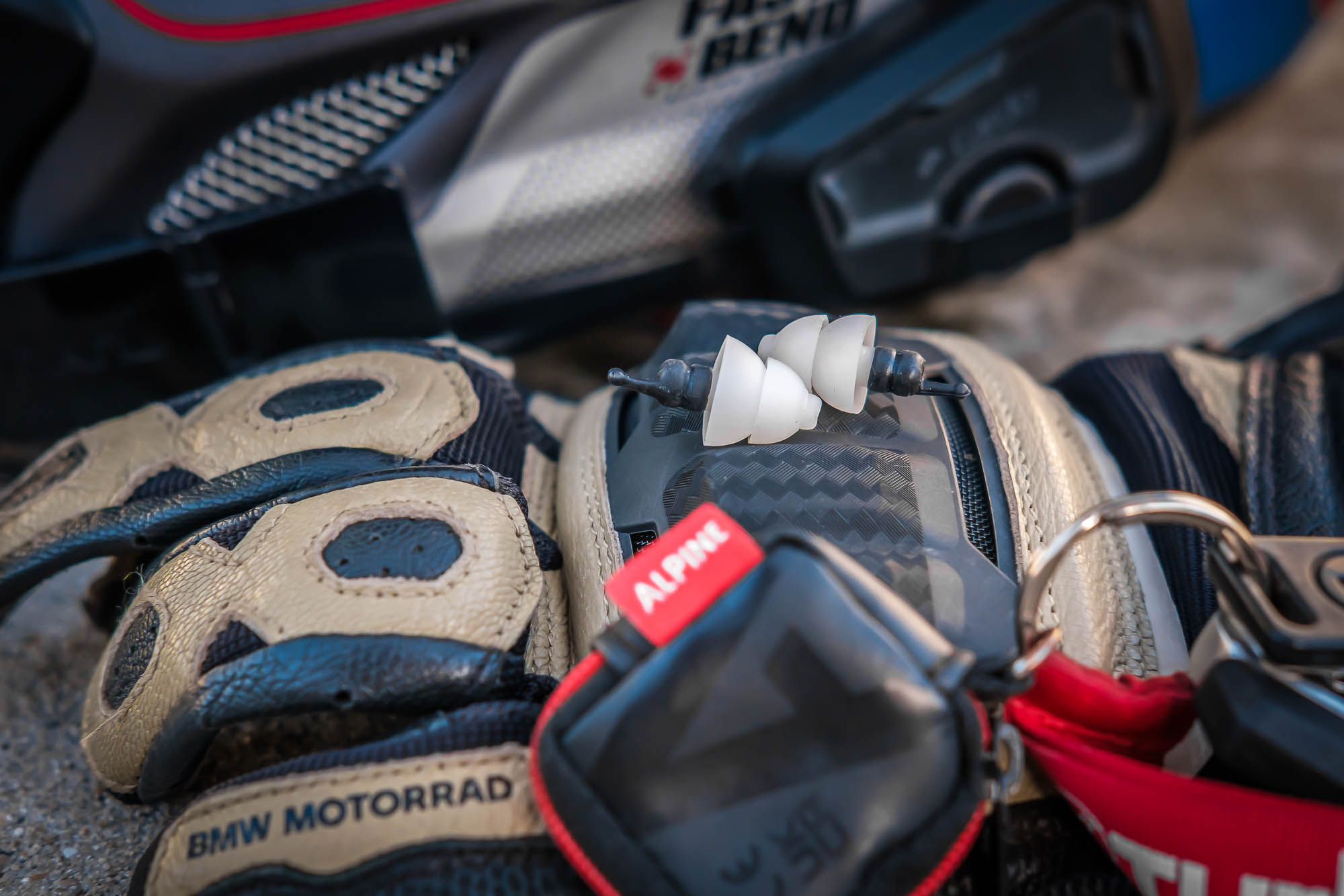Motorcycle riding essentials including Alpine MotoSafe filtered earplugs, riding gloves and motorcycle keys. Wearing motorcycle earplugs helps reduce wind noise and protects hearing on long rides.